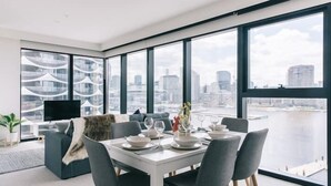 Een moderne eetruimte met een witte tafel gedekt voor zes personen, grote ramen met uitzicht op de stad en het water.