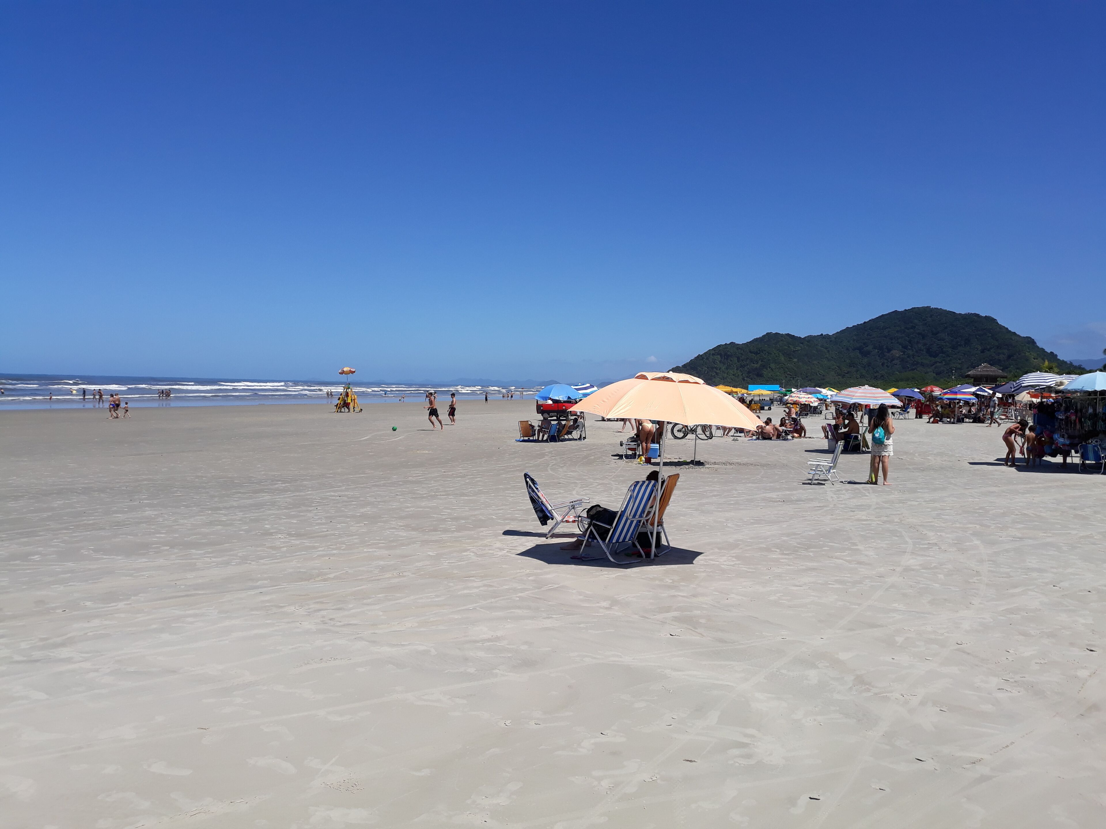 Ein Strand mit Sonnenschirmen, Liegestühlen und Menschen.