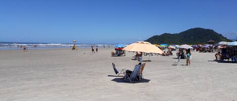 Ein Strand mit Sonnenschirmen, Liegestühlen und Menschen.