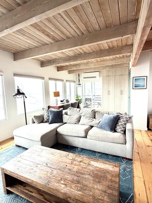 Una sala de estar con un sofá seccional, una mesa de centro de madera y un techo con vigas a la vista.