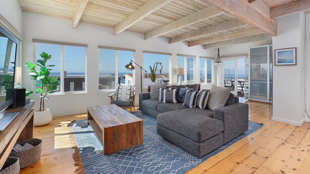 Amplia sala de estar con un sofá grande de color gris, una mesa de centro de madera y vistas al océano a través de amplias ventanas.