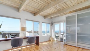Una habitación amplia con suelo de madera, ventanas grandes, un escritorio, dos sillas y vista al mar.