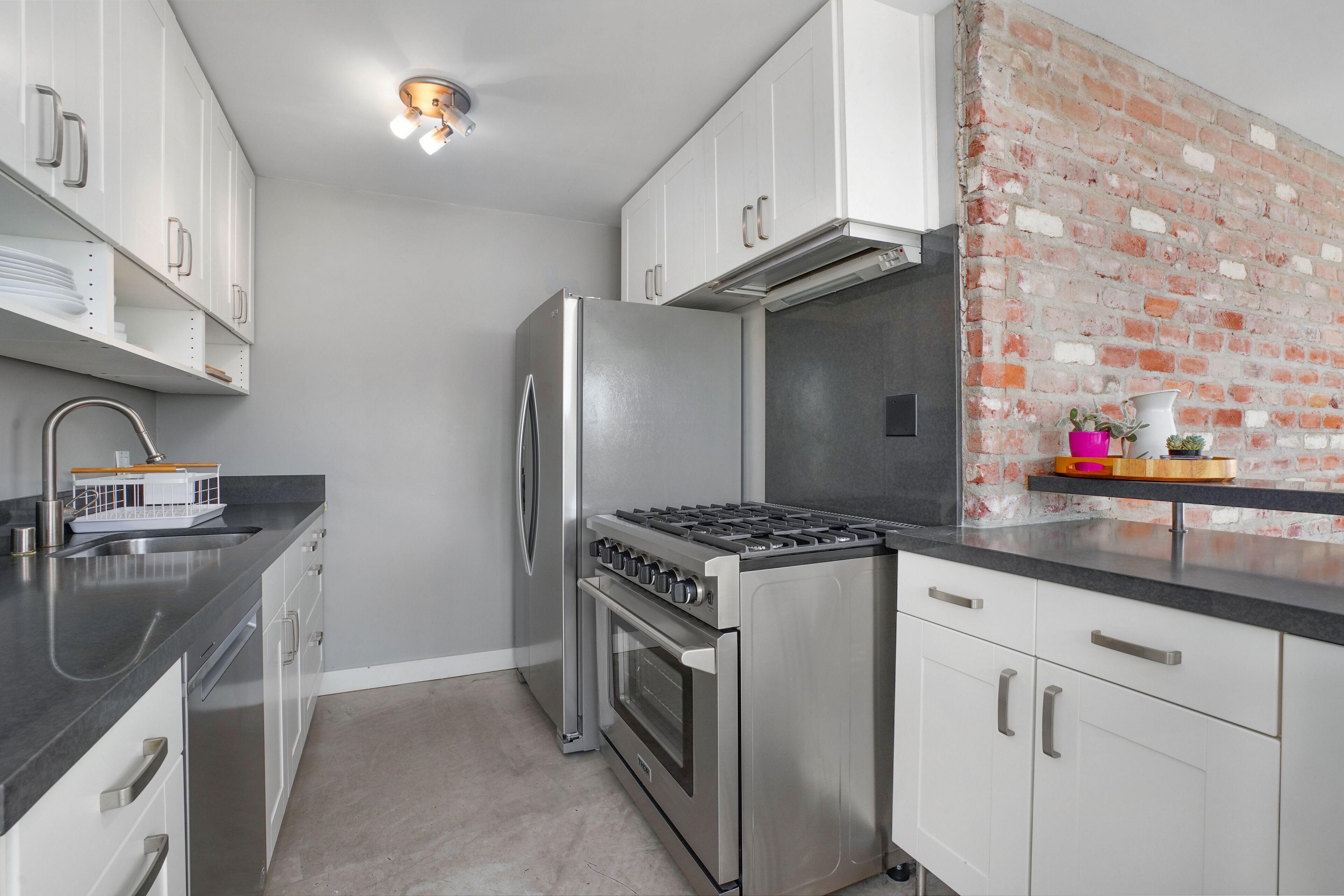 Una cocina moderna con electrodomésticos de acero inoxidable, armarios blancos y una pared de ladrillo decorativa.
