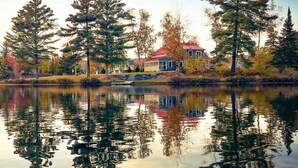 Une propriété située au bord d’un lac, avec une maison dotée d’un toit rouge, entourée de grands arbres et bordée d’une étendue d’eau calme qui reflète le paysage.