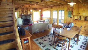 L’intérieur d’un chalet en bois comprend une cheminée, une table à manger et un coin salon confortable avec un canapé et des fauteuils.