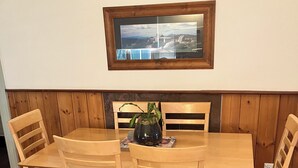 Un coin repas avec une table et des chaises en bois, un vase avec une plante et deux tableaux encadrés au mur.
