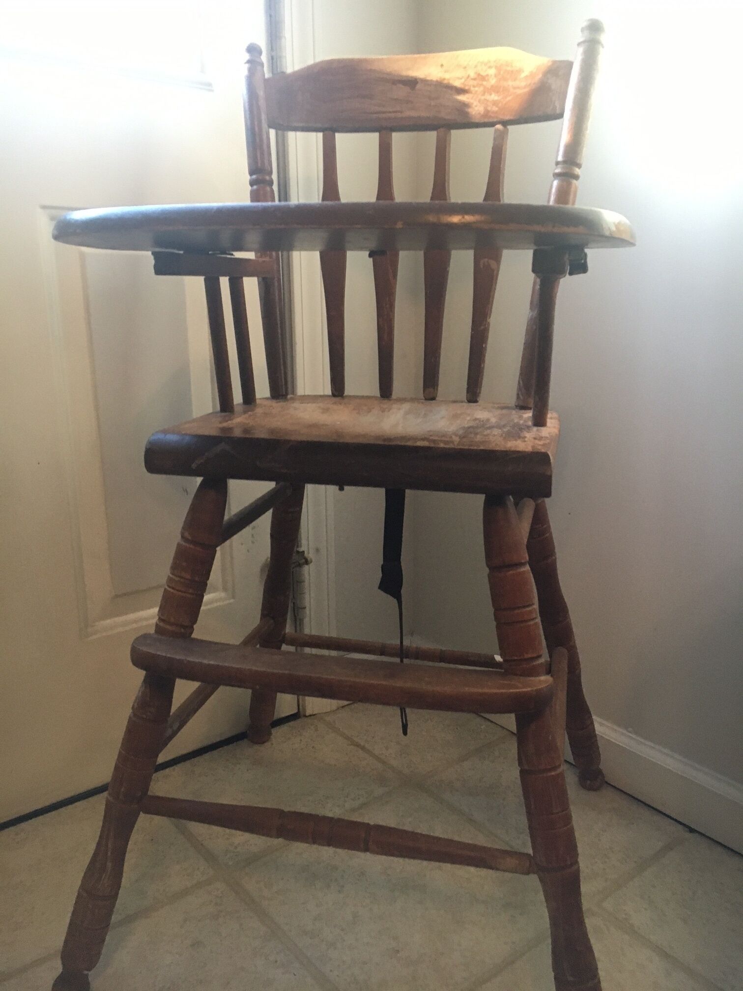 A wooden chair with a high backrest and a cushioned seat, positioned in a room with a tiled floor and a white door in the background.