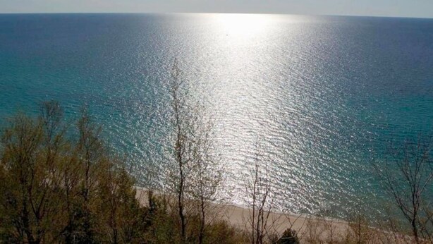 Una playa con agua azul cristalina y un sol brillante reflejándose en la superficie.