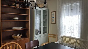 Un comedor con una mesa de madera, sillas, un aparador con puertas de cristal y una araña.