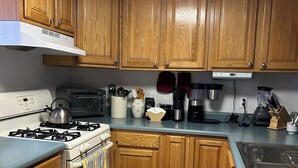 Una cocina con armarios de madera, estufa, microondas, cafetera y licuadora.