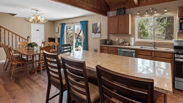 A spacious kitchen with wooden cabinets, a granite countertop, and a large island with chairs. - Moonridge Memories - 5 Bedroom, Hot Tub, Game Room, Pool Table (Big Bear City)