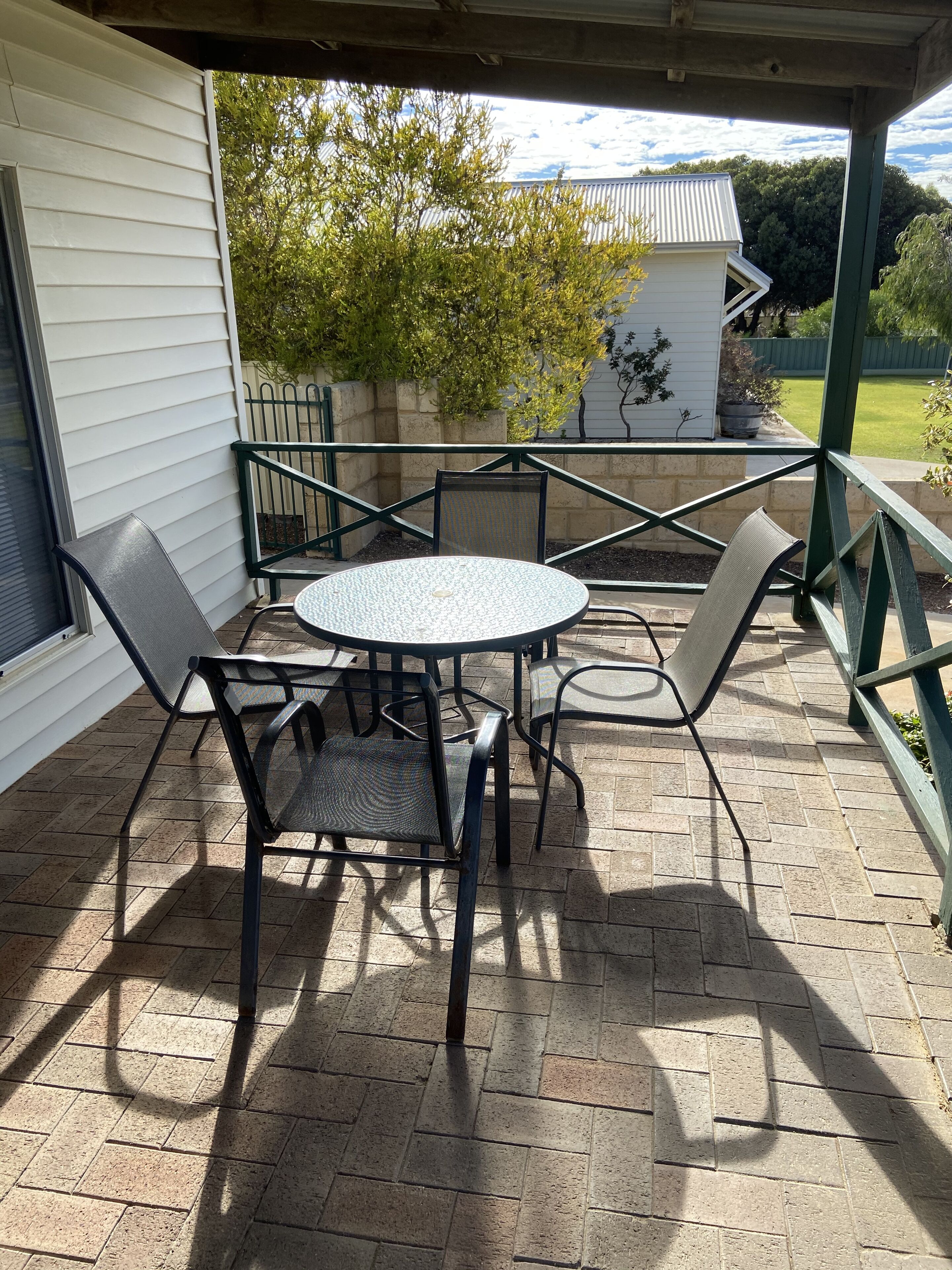 A patio with a round table and four chairs, a brick floor, and a view of a house and trees.