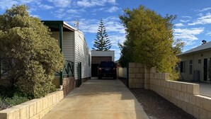 A concrete pathway leading to a garage door, flanked by trees and a brick wall.