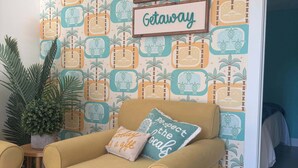 A cozy room with a yellow armchair, a small table with a potted plant, and a wall decorated with a tropical pattern and a sign that reads "anna maria island getaway".