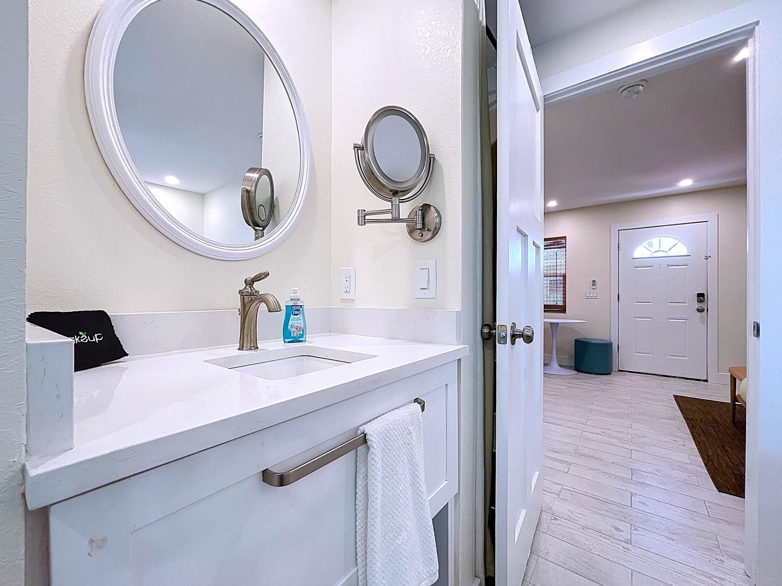 A bathroom with a white vanity, two round mirrors, a faucet, and a bottle of hand soap.