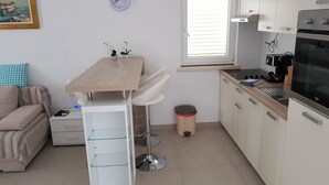 A compact kitchen with a dining table, white cabinets, a stove, and a window with blinds. - suite for relaxing croatia (Korčula)