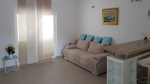A modern living room with a sofa, a small table with a vase of flowers, a dining area with a glass table, and a sliding door leading to a balcony. - suite for relaxing croatia (Korčula)