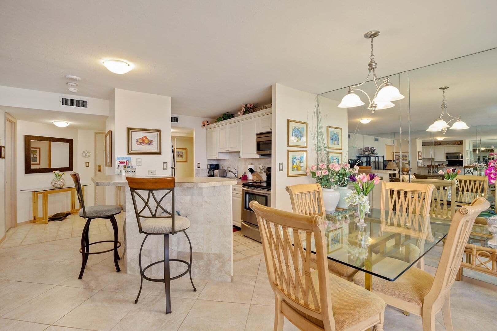 A modern kitchen with a glass dining table, bar stools, and wooden chairs.