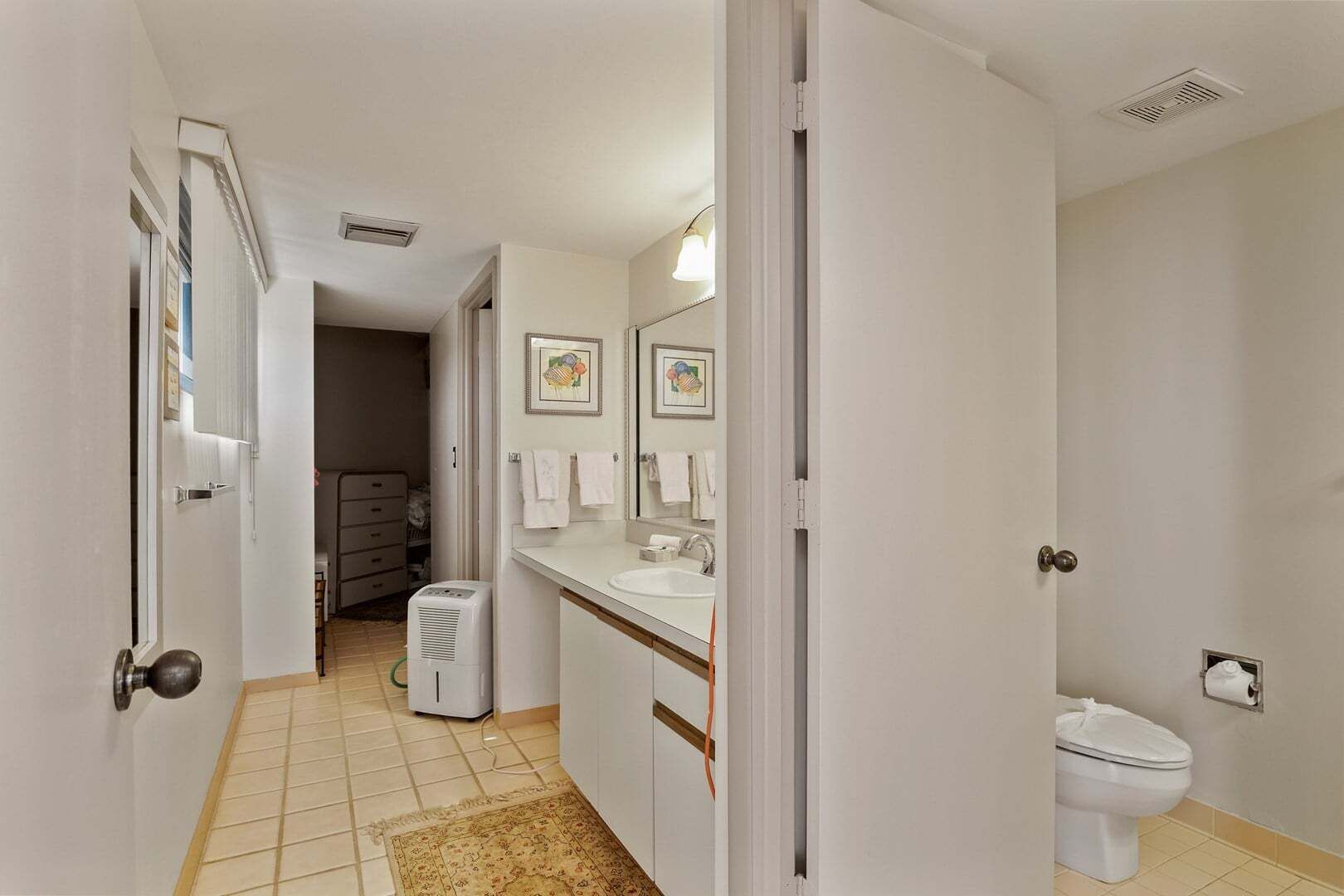 A bathroom with a toilet, sink, and mirror. There is a hallway leading to another room.