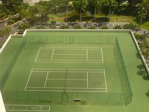 A tennis court with a net and surrounding fence, surrounded by trees and a parking lot. - Beachfront 2BR/2BA condo on Marco Island with heated pool, WiFi and kitchen. (Marco Island)