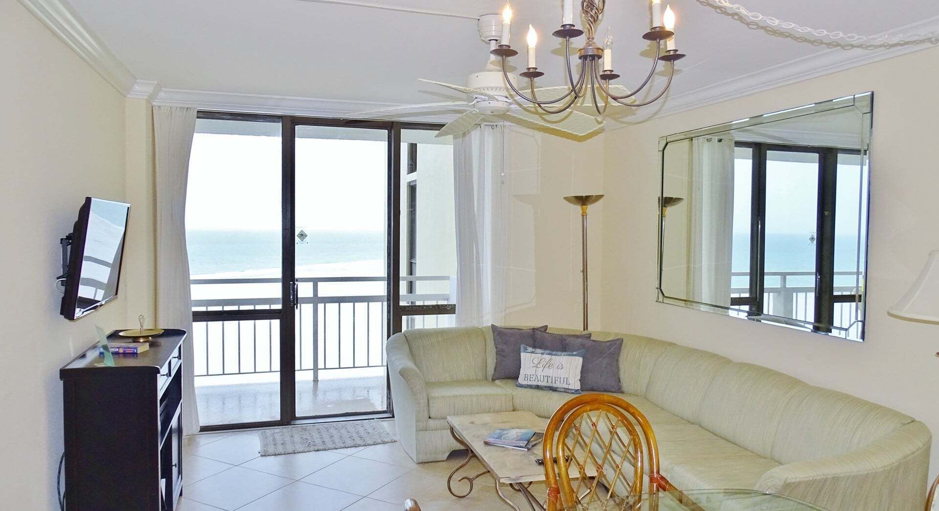 Un soggiorno con divano, poltrona, televisione, lampadario e balcone con vista.