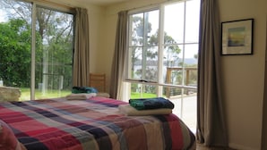 Un dormitorio con una cama grande, una silla y vistas a una terraza y árboles a través de amplios ventanales.