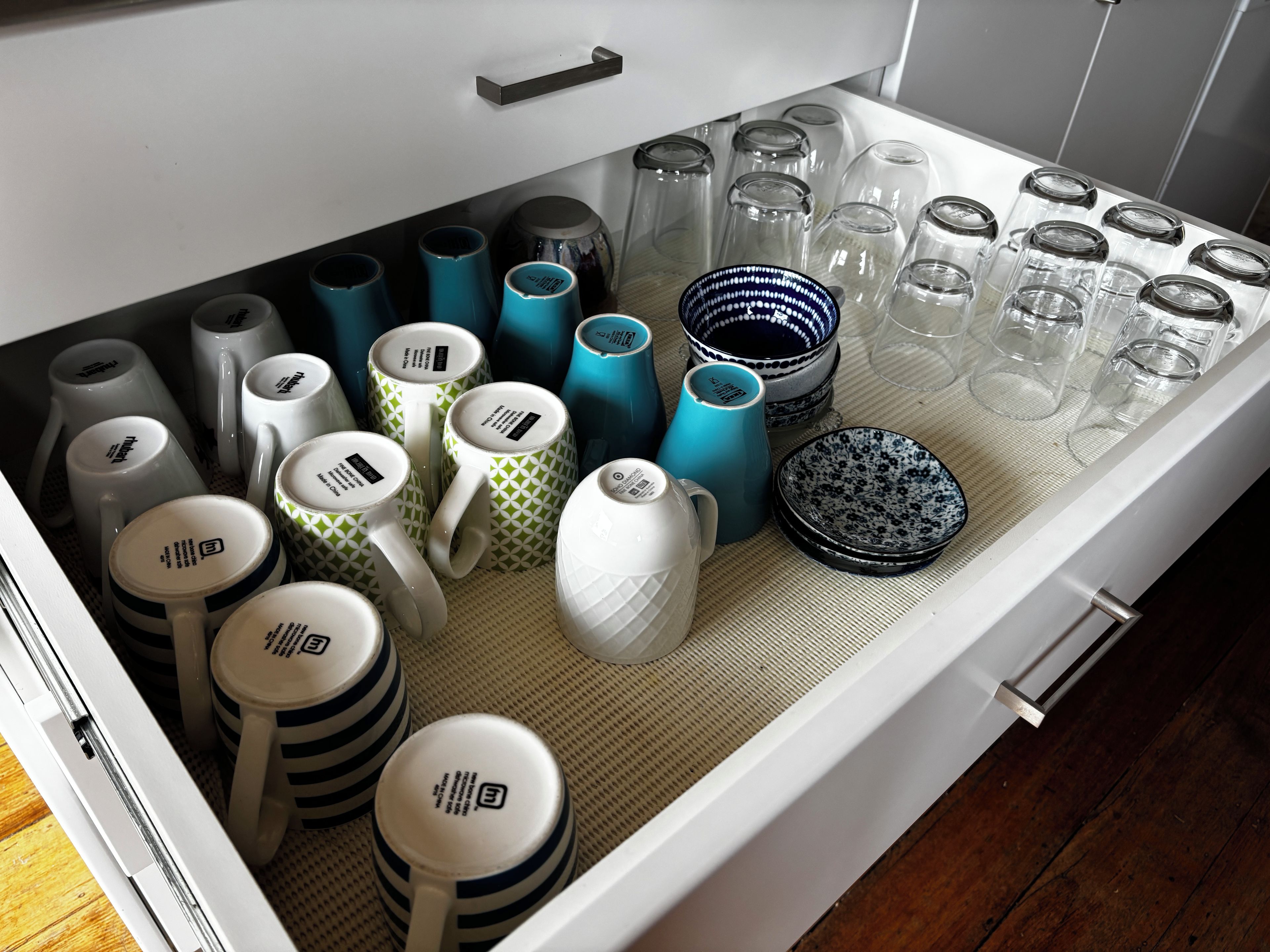 A drawer with various kitchenware items including mugs, plates, and bowls.