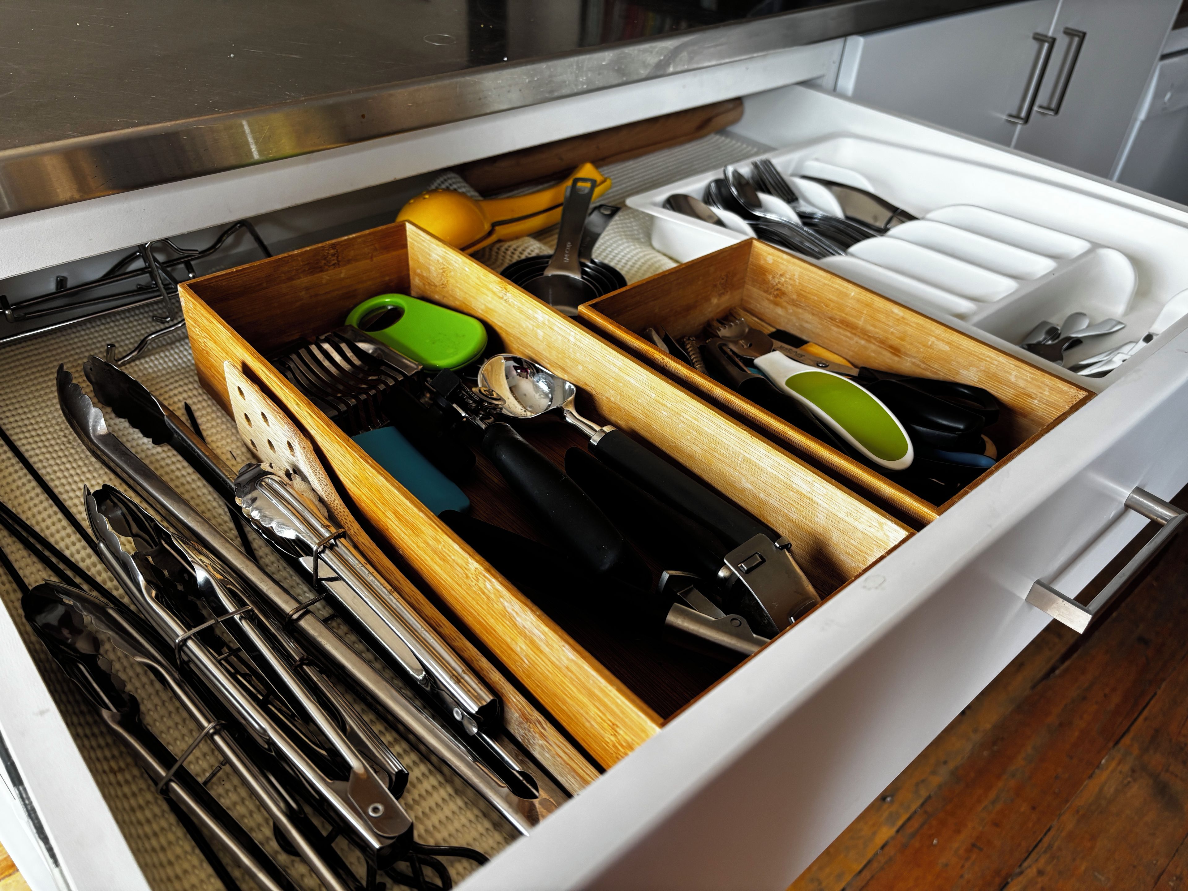 A drawer with various kitchen utensils, including knives, tongs, and a green-handled tool.