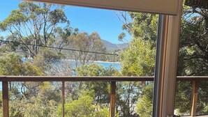 Una habitación con una mesa y una silla de madera, un ventanal con vistas a árboles y una masa de agua.