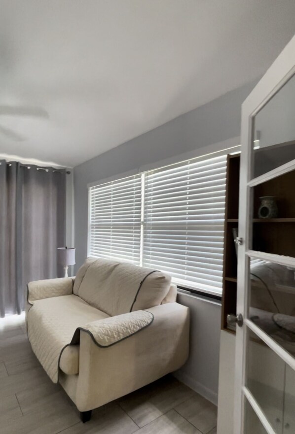Ein Zimmer mit einem beigen Sofa, einer Lampe und einem Fenster mit Jalousien.