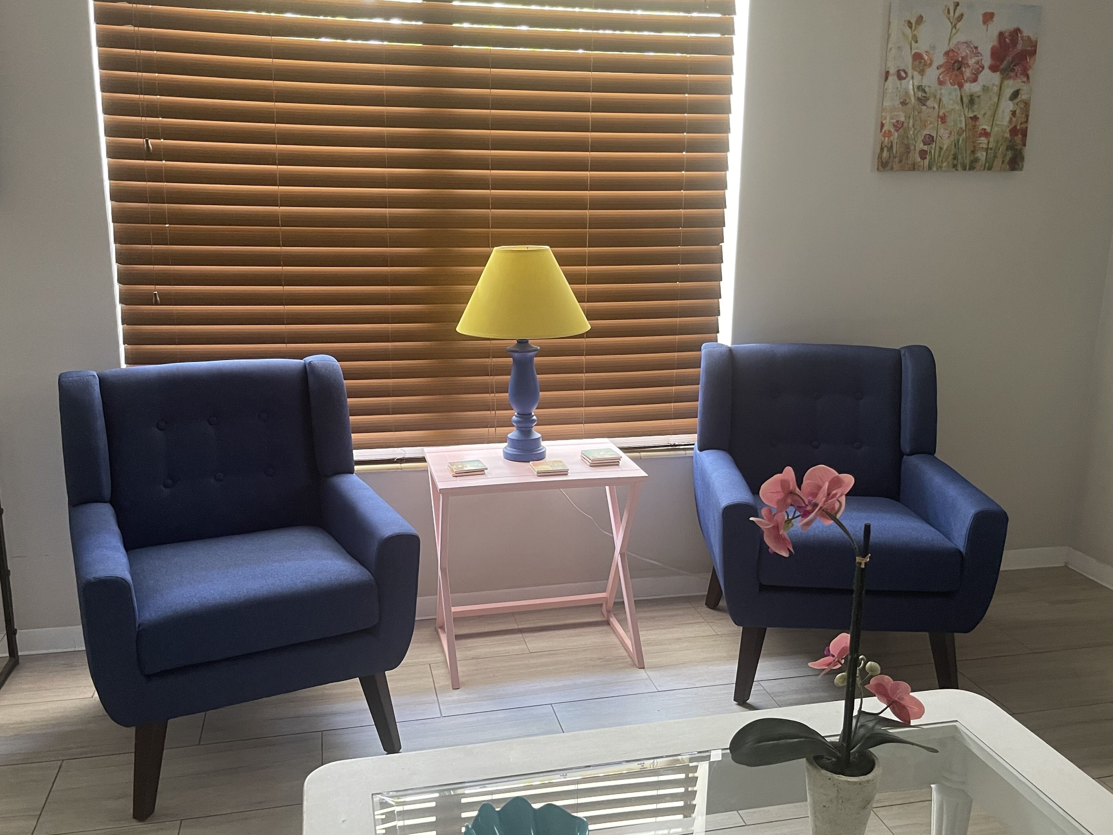 Ein Zimmer mit zwei blauen Sesseln, einem kleinen weißen Tisch mit Lampe und einer Topforchidee.