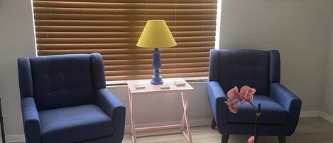 Ein Zimmer mit zwei blauen Sesseln, einem kleinen weißen Tisch mit Lampe und einer Topforchidee.