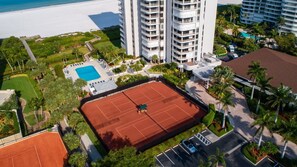 Vue aérienne d’un hôtel avec un court de tennis, une piscine et une plage en arrière-plan.
