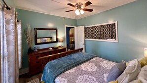 Une chambre à coucher avec un lit, une commode, un miroir et un ventilateur de plafond.