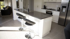 Une cuisine moderne avec des meubles blancs, un réfrigérateur en acier inoxydable et un coin bar équipé de tabourets.