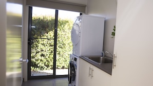 Un espace buanderie comprenant un lave-linge, un sèche-linge, un évier et donnant sur un espace verdoyant grâce à une porte vitrée.