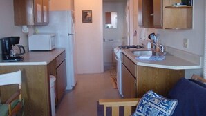 Une cuisine de taille réduite, avec des meubles en bois, un réfrigérateur blanc, un four à micro-ondes, une cuisinière et un évier.