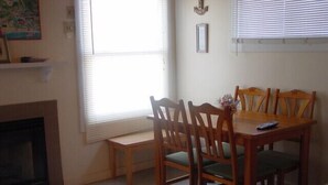 Un coin repas avec une table et des chaises en bois, une cheminée et une fenêtre équipée de stores.