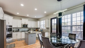 Uma cozinha moderna com armários brancos, uma ilha central e um espaço de jantar com mesa e cadeiras de vidro.