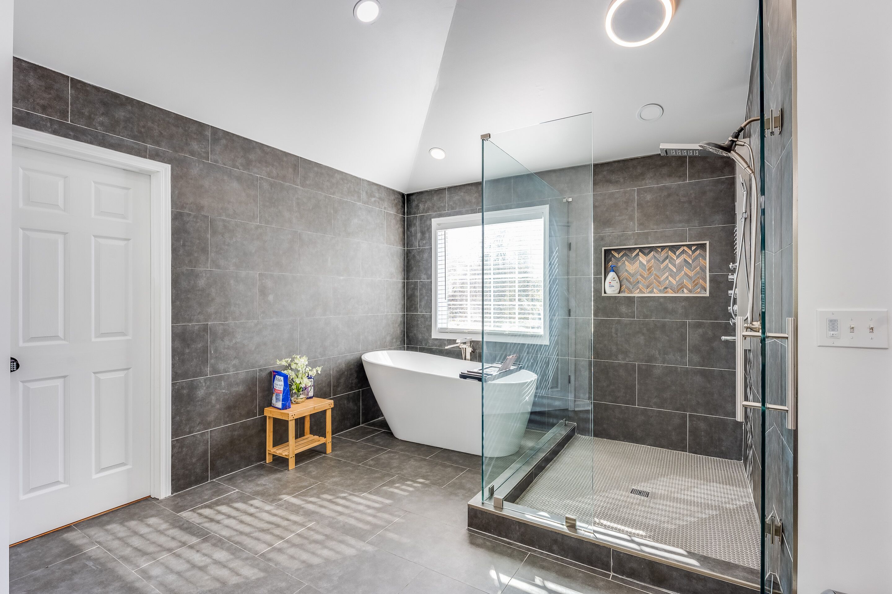 A modern bathroom with a freestanding bathtub, a glass-enclosed shower, and a small wooden stool with toiletries.