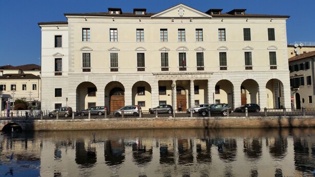Un edificio grande e histórico con múltiples arcos y una masa de agua que se refleja.