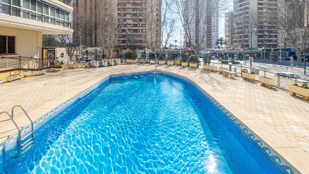 A swimming pool with a tiled edge, surrounded by a tiled deck and a low wall.