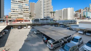 A parking lot with multiple cars, a covered area, and buildings in the background.