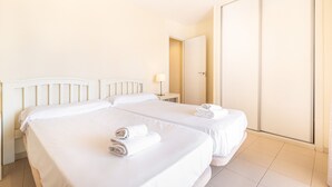 A hotel room with two beds, a nightstand, a lamp, and a sliding door.
