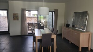 Un comedor moderno con una mesa larga, sillas, un armario y un amplio ventanal con cortinas.