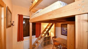 Habitación con literas, un escritorio, una silla, una escalera y una ventana con cortinas.
