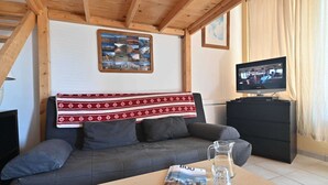 Una sala de estar acogedora con un sofá, un televisor, una revista y una jarra de agua sobre una mesa.