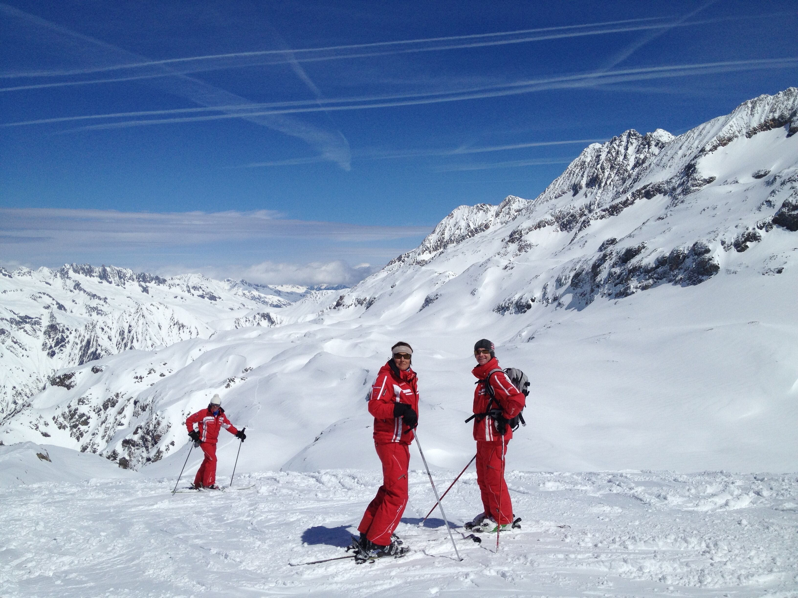 Un paysage de montagne enneigé avec trois skieurs vêtus de tenues rouges.