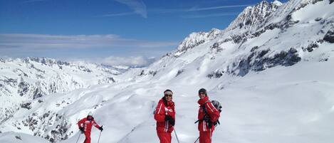 Un paysage de montagne enneigé avec trois skieurs vêtus de tenues rouges.