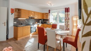 Une cuisine moderne avec des meubles en bois, une table à manger entourée de chaises rouges et une vue sur l’extérieur grâce à de grandes fenêtres.